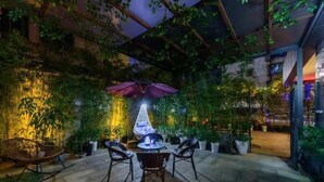 An outdoor patio with a table and chairs, surrounded by potted plants and a decorative umbrella.