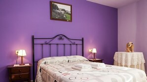 A bedroom with a purple wall, a bed with a patterned bedspread, two bedside lamps, a small table with a teddy bear, and a framed picture on the wall. - Marquet house for 4 people (Valle de Lierp)