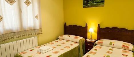 Een hotelkamer met twee bedden, een radiator, een nachtkastje met een lamp en een schilderij aan de muur.