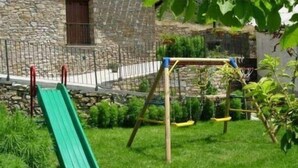 A stone building with a metal fence, a green slide, and a wooden swing set in a grassy yard. - Marquet house for 4 people (Valle de Lierp)