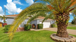 A residential house with a well-maintained lawn, a palm tree, and a garage. - *Tinkerbells Castle 2*  Private Pool & Spa Overlooking Lake & Disney Fire Works (kissimmee)