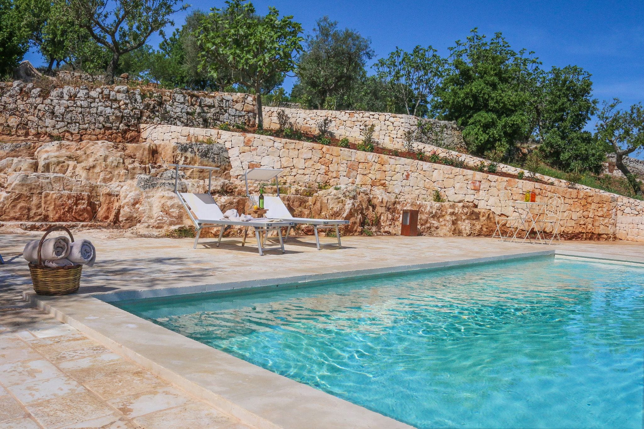 A pool area with stone walls, lounge chairs, and a clear blue pool.