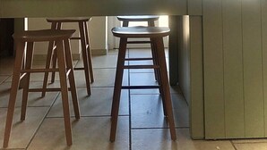 A kitchen with a large window, wooden stools, and a hanging light fixture.