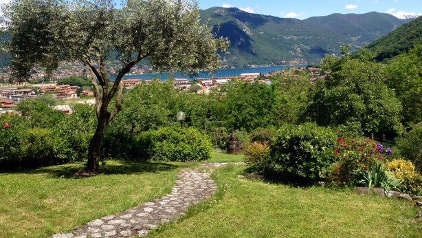 A stone pathway leading through a lush garden with a view of a town and mountains in the background.