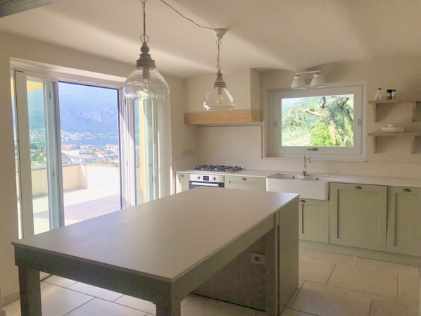A modern kitchen with a large island, a gas stove, and a window with a view of the outdoors.