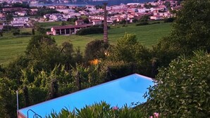 A residential area with a swimming pool surrounded by greenery and a distant view of a town and mountains.