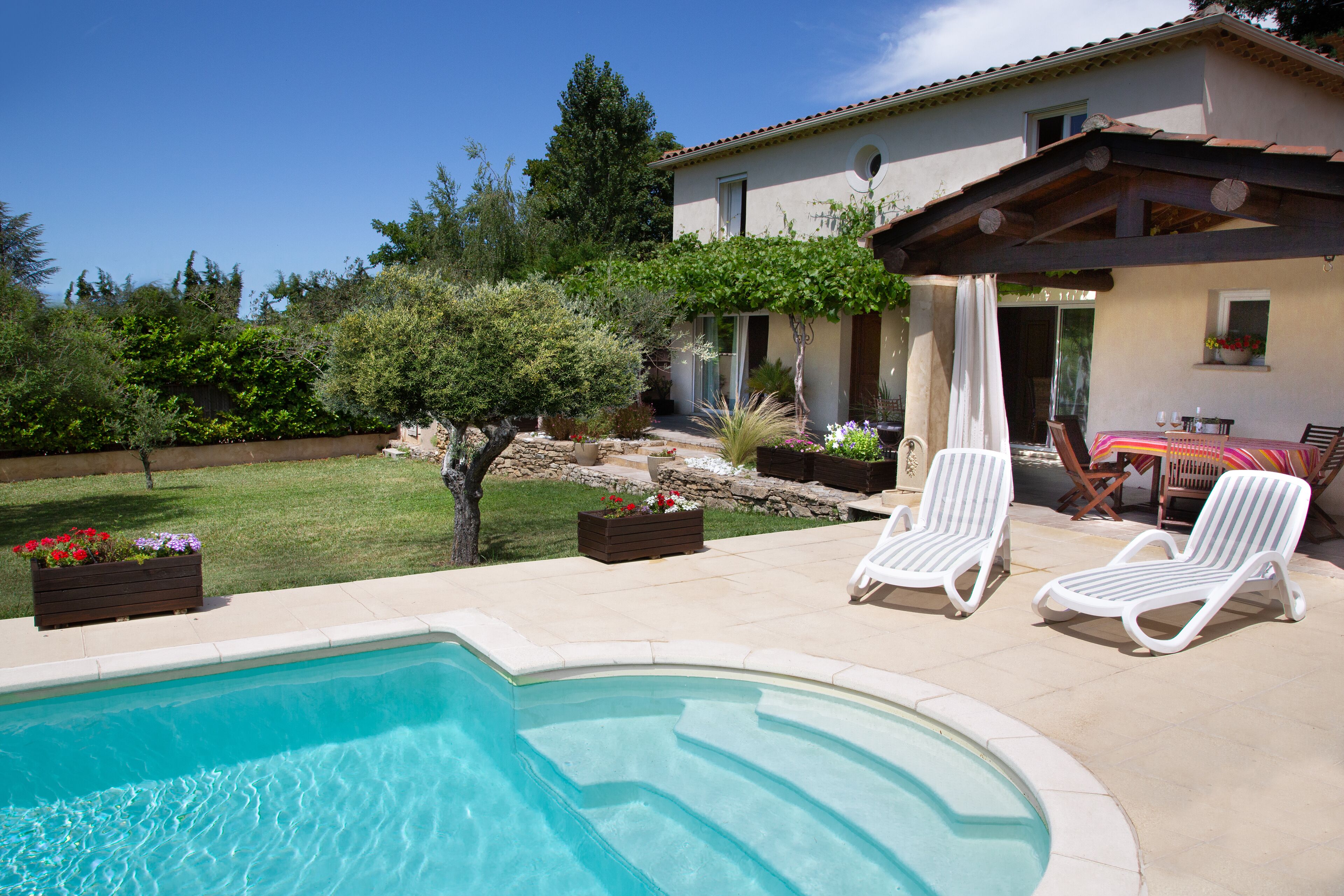 A swimming pool with two lounge chairs and a patio area with a table and chairs.