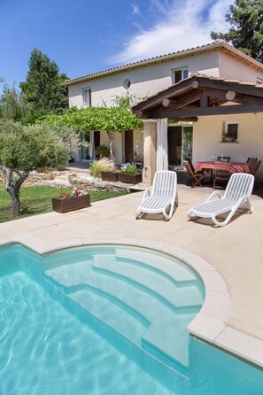 Una piscina con sillas de descanso, un patio y una casa con techo de tejas.