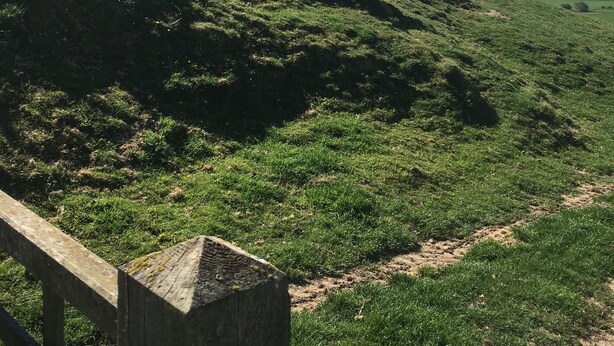 Une colline herbeuse avec une clôture en bois au premier plan.