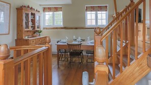 Un espace repas avec des meubles en bois, un escalier et une fenêtre donnant sur un paysage verdoyant.