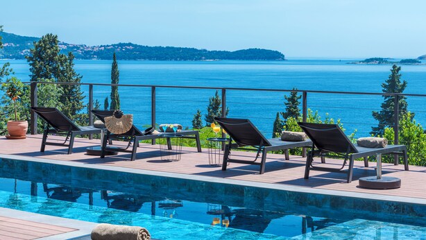 Zona de piscina con sillas de descanso y vista al mar.