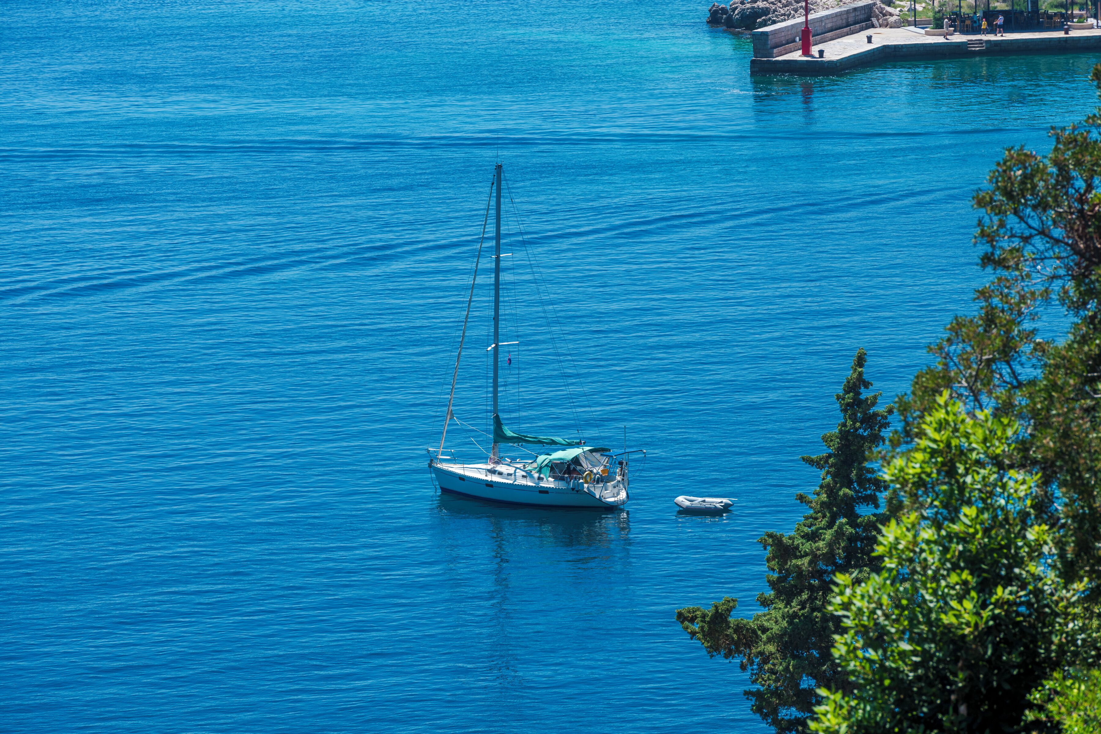 Eine Segelyacht liegt in ruhigem, blauem Wasser, in der Nähe befindet sich ein kleines Boot.