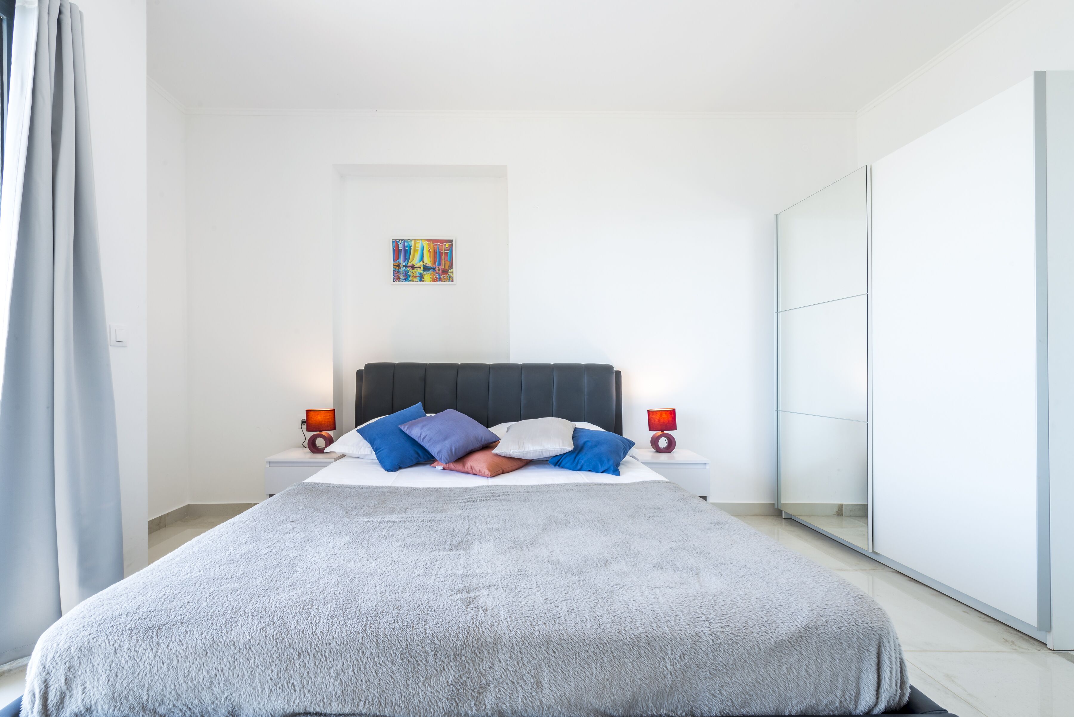 Un dormitorio moderno con una cama grande, un cabecero, mesitas de noche con lámparas, una obra de arte colorida en la pared y una puerta de armario corredera.