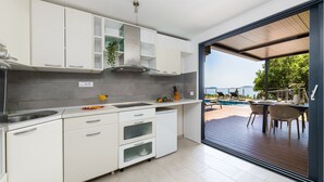 Una cocina moderna con armarios blancos, horno integrado y vista a una terraza exterior con piscina y sillas de descanso.