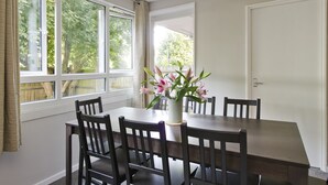 A dining area with a table and chairs, a vase with flowers, and large windows with curtains. - Spacious Notting Hill Flat (London)