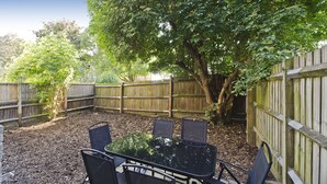 An outdoor patio with a glass-top table and four chairs, surrounded by a wooden fence and trees. - Spacious Notting Hill Flat (London)