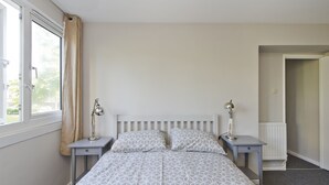 A bedroom with a bed, two bedside tables with lamps, a window with curtains, and a radiator. - Spacious Notting Hill Flat (London)
