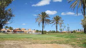 A golf course with palm trees, a clear sky, and buildings with red roofs in the background. - Luxury 2 Bedroom Bungalow With Communal Pool & Wifi On Golf Resort (Antigua)