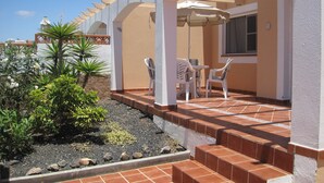A patio area with a white pergola, outdoor seating, and a small garden with plants and rocks. - Luxury 2 Bedroom Bungalow With Communal Pool & Wifi On Golf Resort (Antigua)