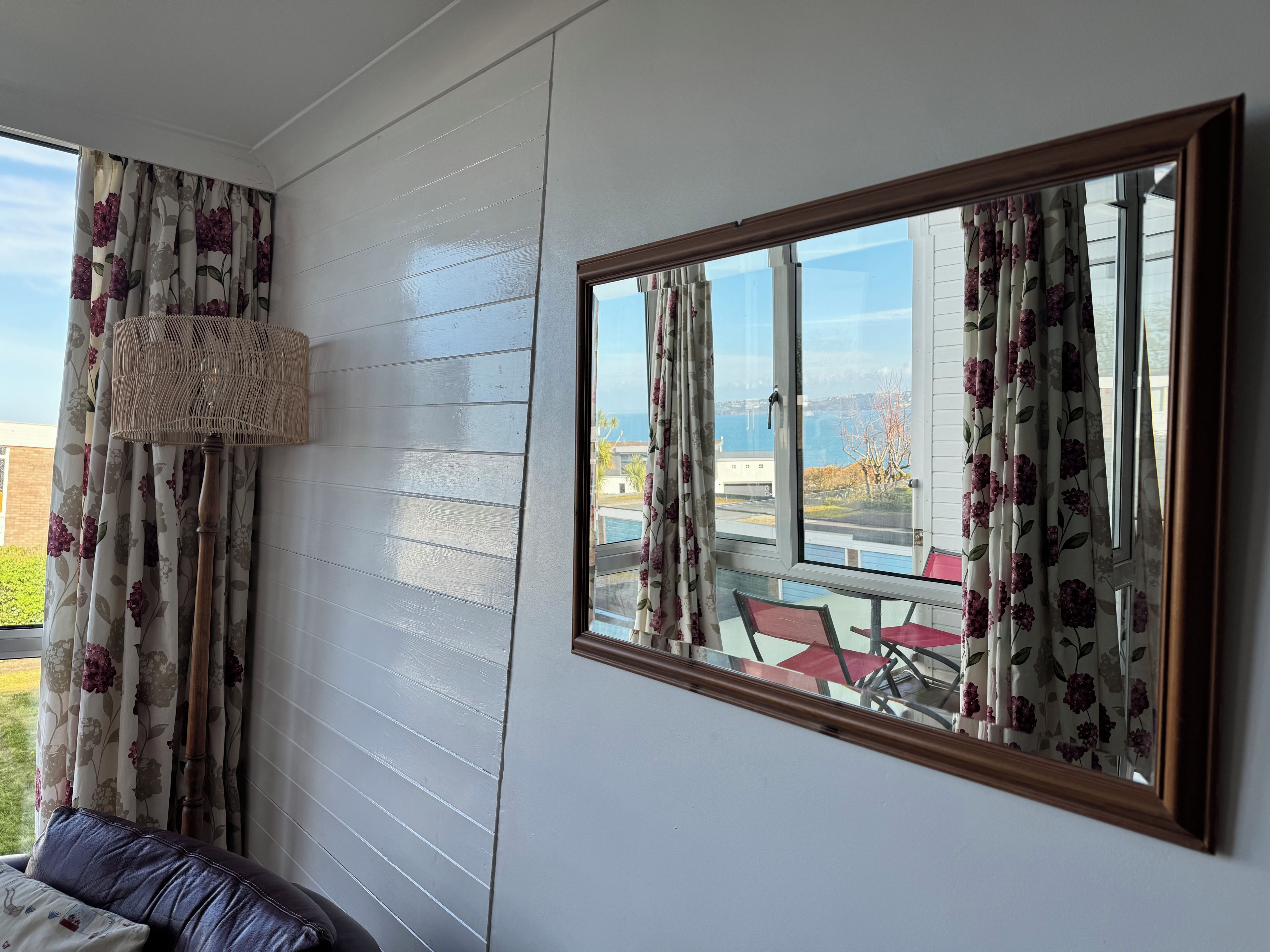 A room with a large window, a mirror, and a sofa.