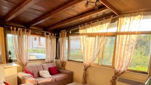 Ein geräumiges Wohnzimmer mit einer Sofagarnitur, einem Couchtisch und großen Fenstern mit Vorhängen.