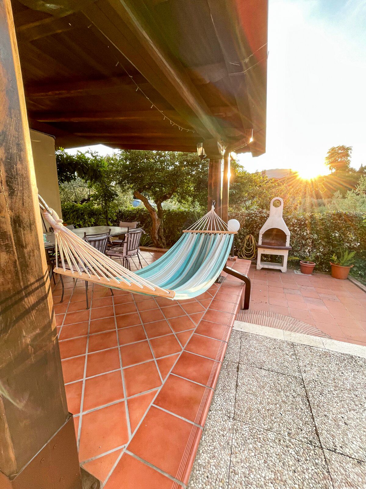 Un hamac sous une pergola en bois, un coin salon extérieur rustique avec un sol en briques et une cheminée en pierre.