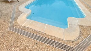 Ein Swimmingpool mit einer gefliesten Kante, umgeben von Liegestühlen und einem roten Sonnenschirm.