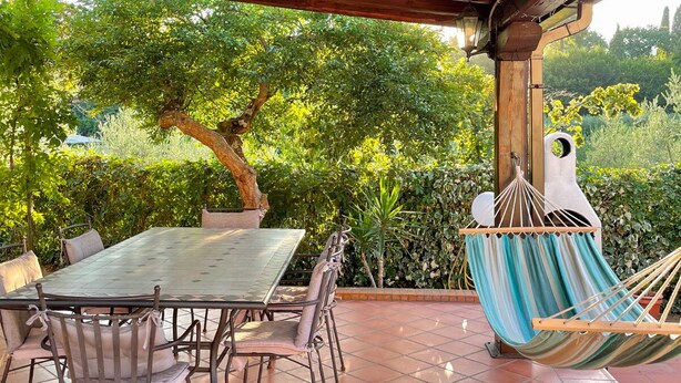 Eine überdachte Terrasse mit Tisch, Stühlen und einer Hängematte, mit Blick auf Grünflächen.