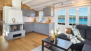 Una cucina moderna con mobili grigi, un piano di lavoro bianco e un camino integrato. Si vede un'ampia finestra con vista sul mare.