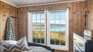 Una camera da letto con una grande finestra, pareti in legno, un letto con coperta fantasia e un comò con cassetti.