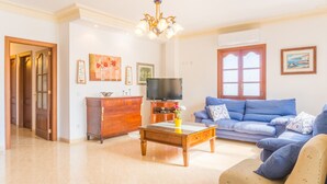 A living room with a blue sofa, a wooden coffee table, a TV, and a chandelier. - Apartamento cerca de la playa Can Berenguer (Port d´Alcudia)