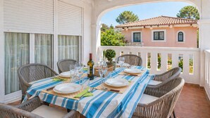 A dining area with a table set for four, wicker chairs, a striped tablecloth, and a view of a building with a tiled roof. - Apartamento cerca de la playa Can Berenguer (Port d´Alcudia)