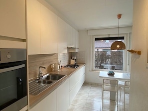 A modern kitchen with white cabinets, stainless steel appliances, and a window with a view of a snowy landscape. - Maison de Marcel - Big family house near city centre- free parking/free bikes (Brugge)