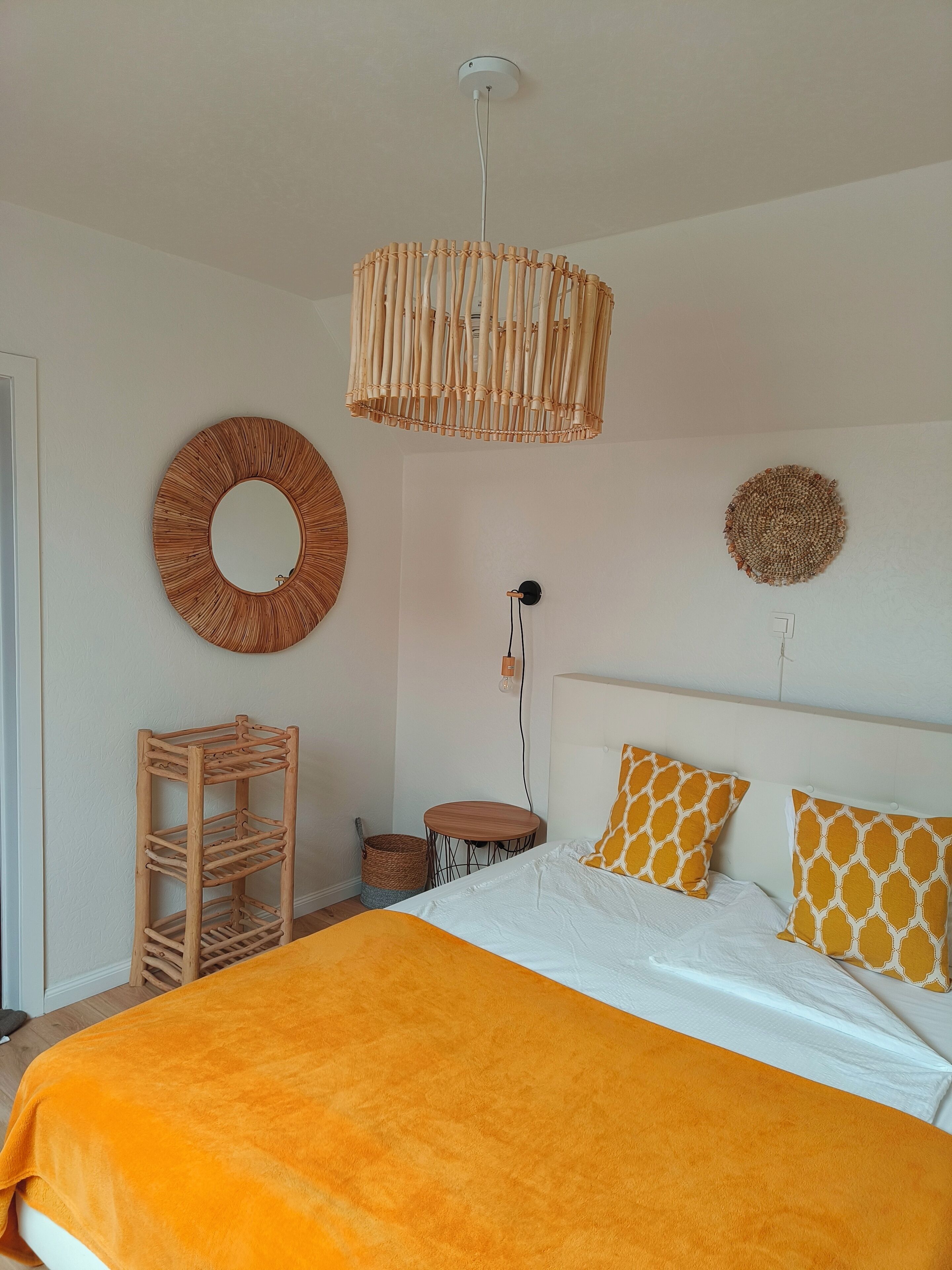 A bedroom with a bed, a bedside table, a hanging light fixture, and wall decor.