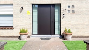 Un bâtiment avec une porte noire, portant le numéro 103, et deux plantes en pot de chaque côté.