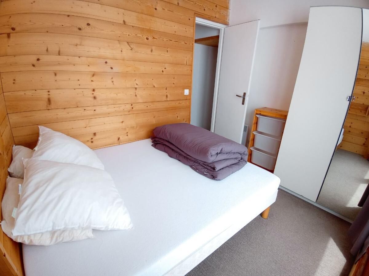 Een enkel bed met wit en paars beddengoed, een houten hoofdbord en een witte garderobe met een ladder.