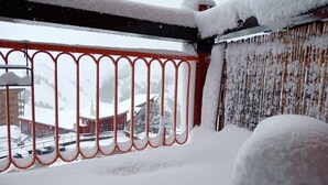A snowy balcony with a red railing, a wooden chair, and a view of buildings and snow-covered streets. - Apartment/ flat - LES ARCS 2000 (Bourg-Saint-Maurice)