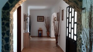 A hallway with a stone archway, a tiled floor, a wooden cabinet, a small table with a vase, and a potted plant.