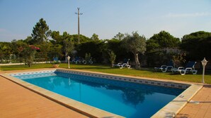 A rectangular swimming pool with a tiled edge, surrounded by a brick patio and a grassy area with lounge chairs.