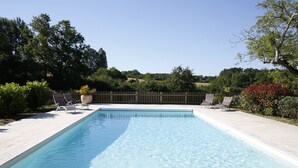 Une piscine rectangulaire à l’eau d’un bleu limpide, entourée d’une clôture en bois et agrémentée de diverses plantes.