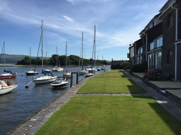 A marina with boats docked along a grassy pathway beside a building with multiple windows.