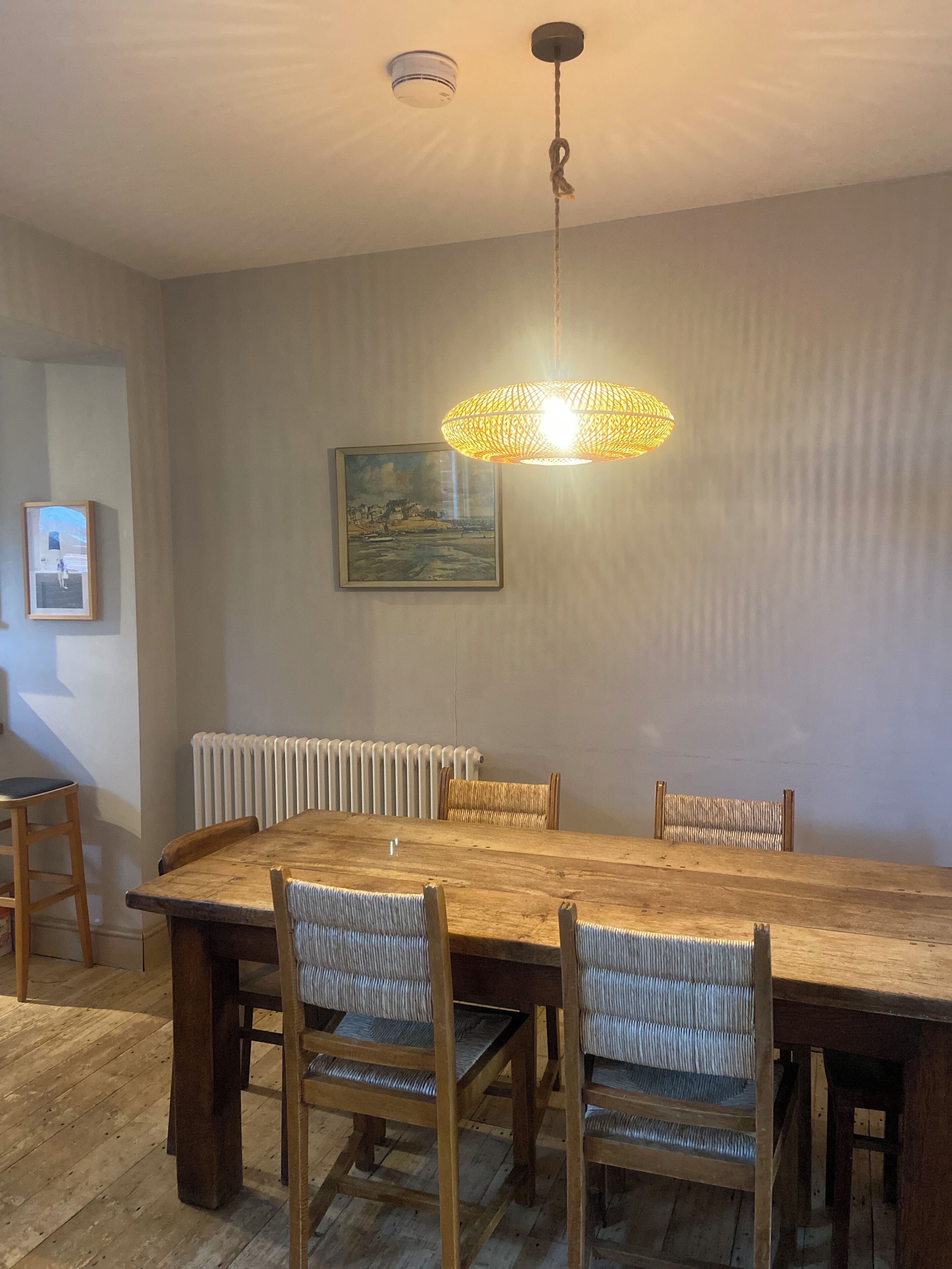 Un coin repas avec une table et des chaises en bois, un luminaire suspendu, un radiateur et un tableau encadré au mur.
