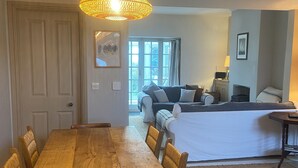 A dining area with a wooden table and chairs, a hanging light fixture, and a sofa in the background. - Coastguard Cottage With Sea Views (fairlight)