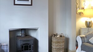 A cozy room with a fireplace, a framed picture on the wall, a wicker basket, and a bed with a plaid blanket. - Coastguard Cottage With Sea Views (fairlight)