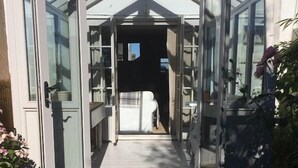 A conservatory with glass doors leading to a pathway. - Coastguard Cottage With Sea Views (fairlight)