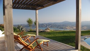 Um deck de madeira com espreguiçadeiras com vista para uma paisagem deslumbrante, incluindo montanhas e um lago.