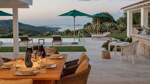 Un espace extérieur aménagé pour les repas, avec vue sur l’océan, une piscine et une pergola dotée de parasols.