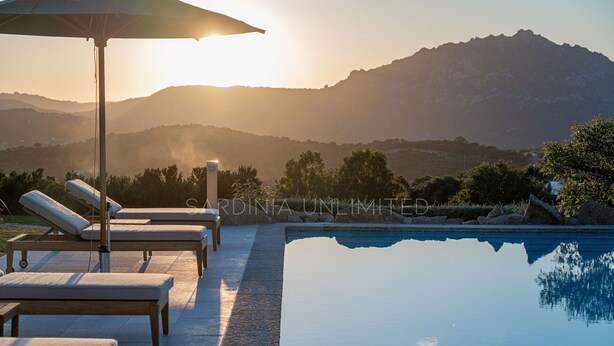 Un espace aménagé au bord de la piscine, avec des chaises longues et un parasol, offrant une vue sur une chaîne de montagnes.