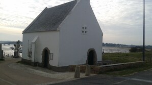 A small white building with a steep roof, two arched doorways, and a small window. -  In a green setting close to the ocean  (Saint-Molf)