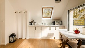 A modern kitchen with white cabinets, a skylight, a dining table, and a view of trees through the window. -  In a green setting close to the ocean  (Saint-Molf)